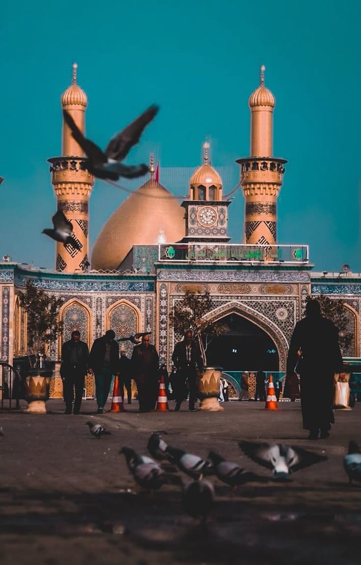 Golden domes and minarets of a mosque under a teal sky with pigeons in flight.