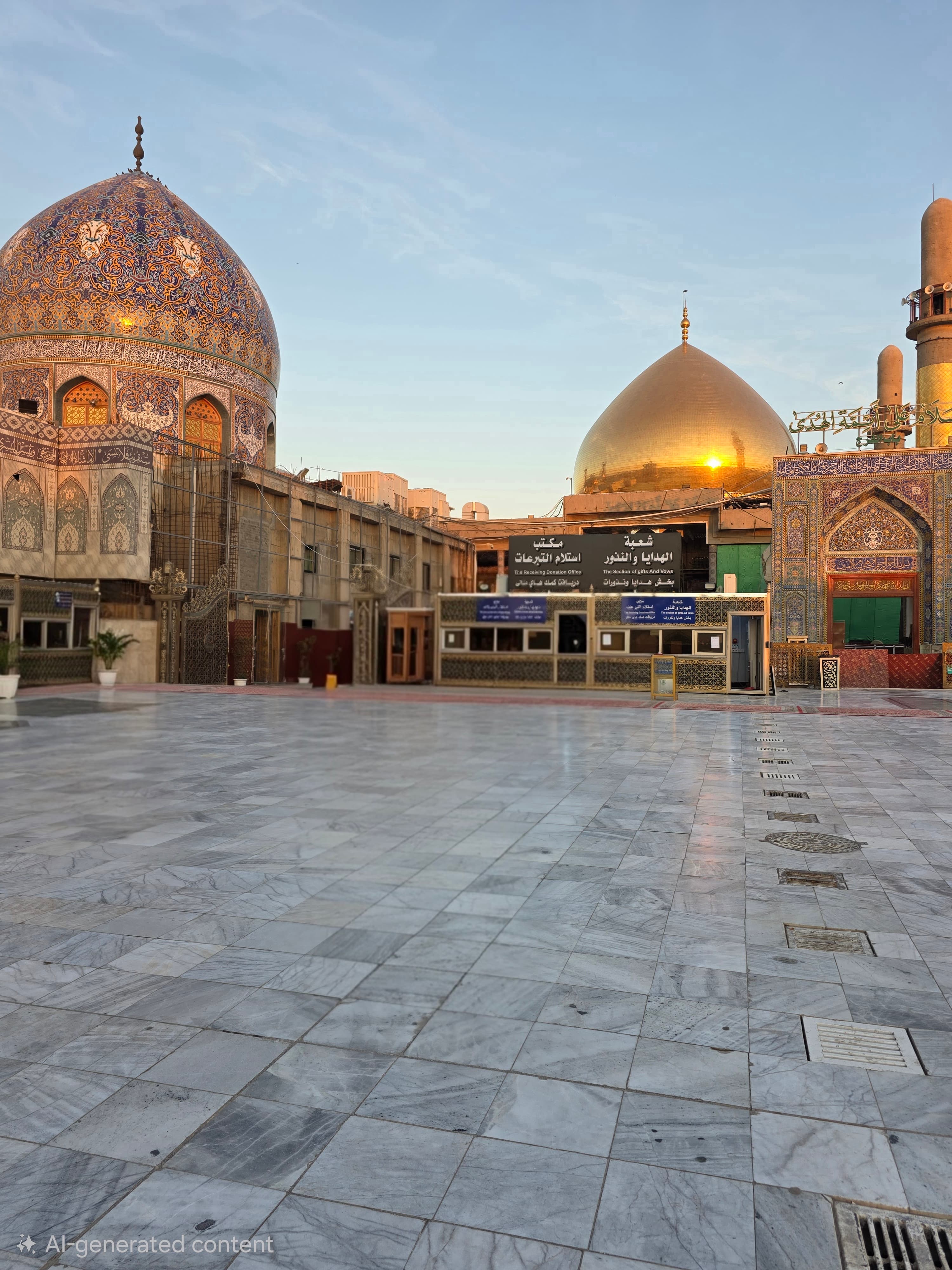 Marble courtyard facing a mosque with a patterned blue dome and a large golden dome.