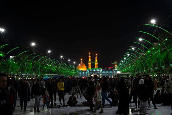 Crowds gather at night in a plaza with green lights leading to a golden shrine.